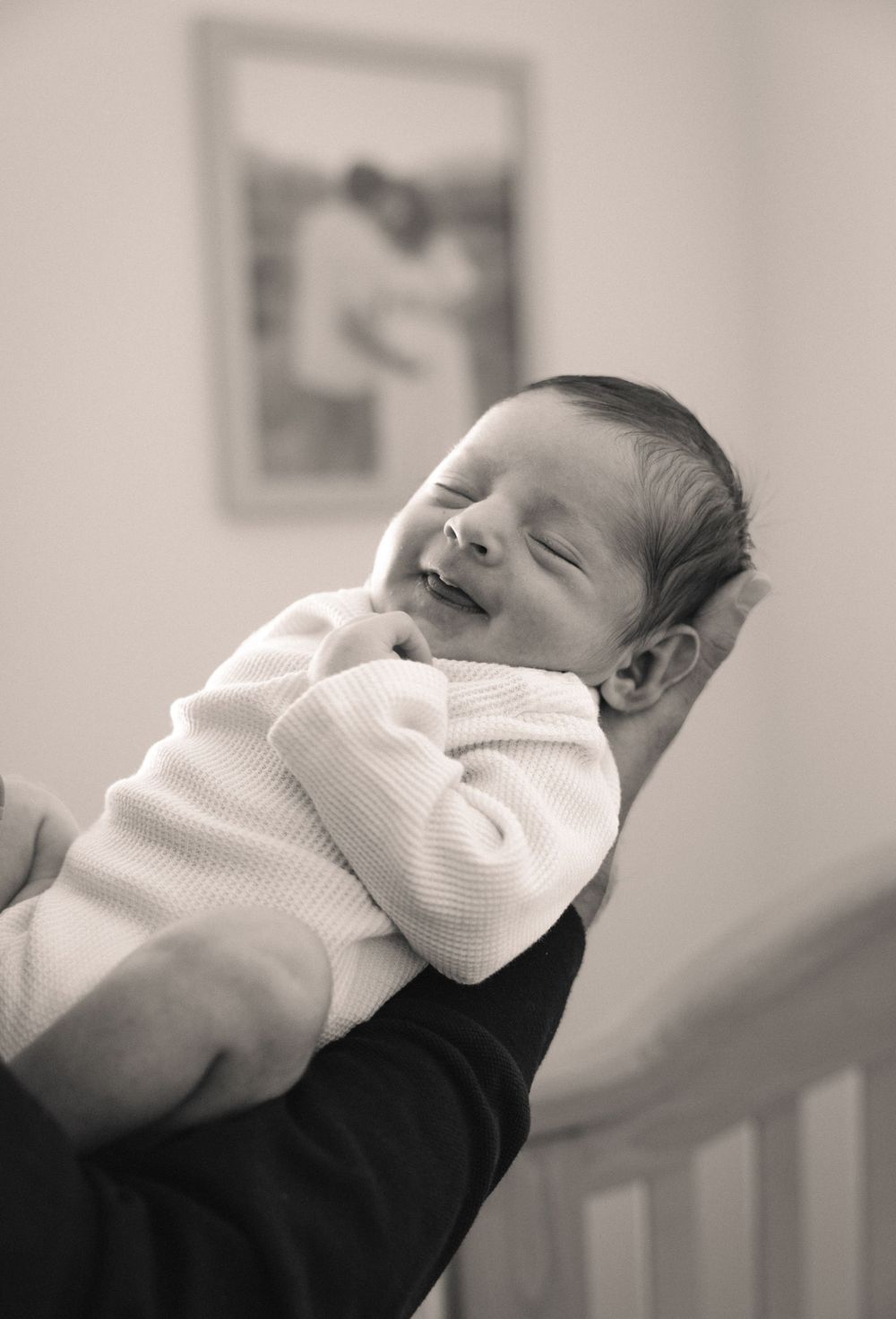 Black and white portrait of a peaceful smiling newborn baby being held gently in loving arms.