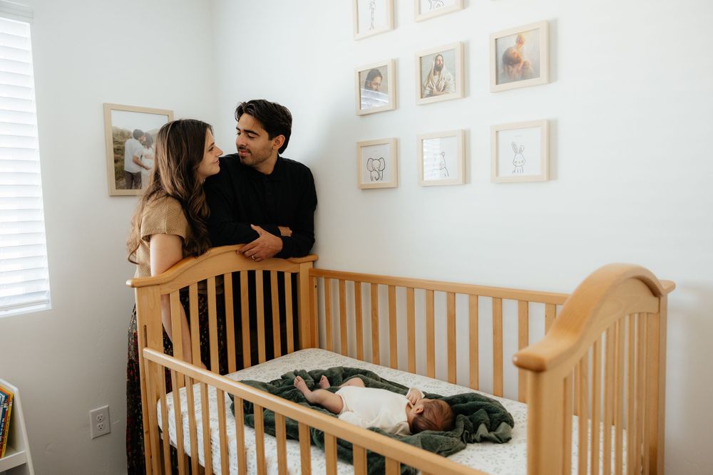 New parents sharing a loving moment beside their sleeping newborn in a wooden crib in the nursery.