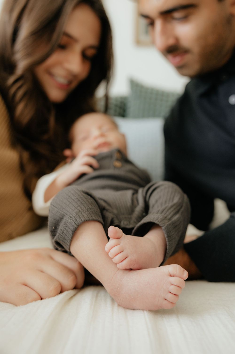 New parents smiling and admiring their newborn baby's tiny feet during an in-home lifestyle photo session.