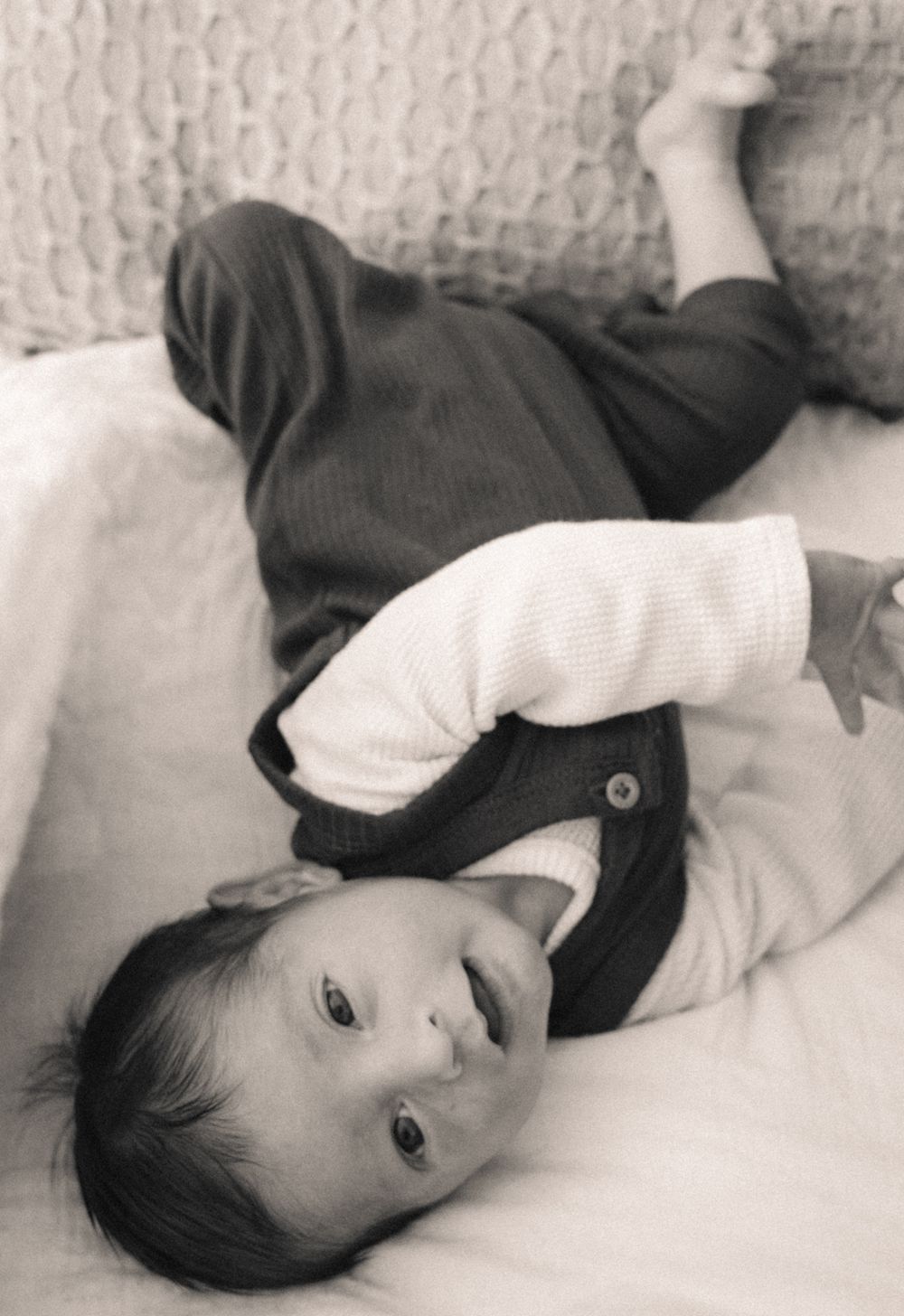 Black and white portrait of an alert newborn baby lying on a soft white blanket looking up curiously.