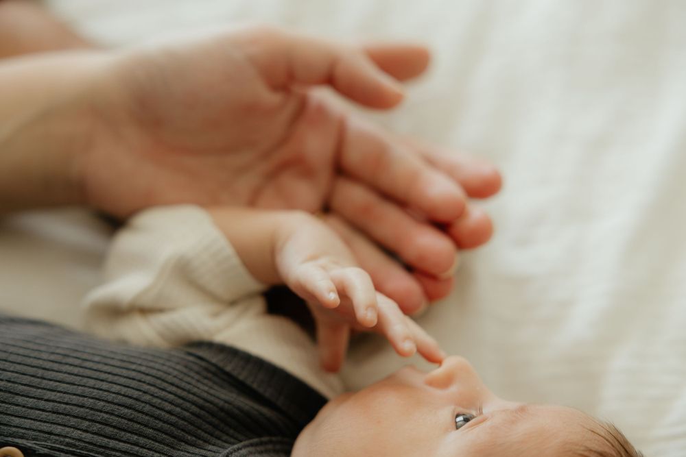 A newborn baby gently grasps an adult finger, showcasing the tiny delicate hands of a new infant.