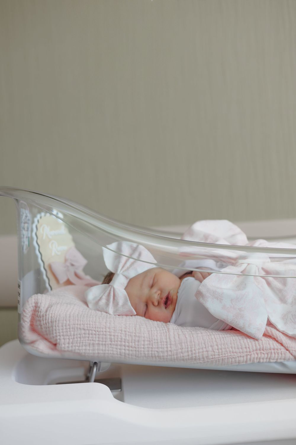 A series of five connected images showing a sleeping newborn baby in white clothing on a light-colored surface.