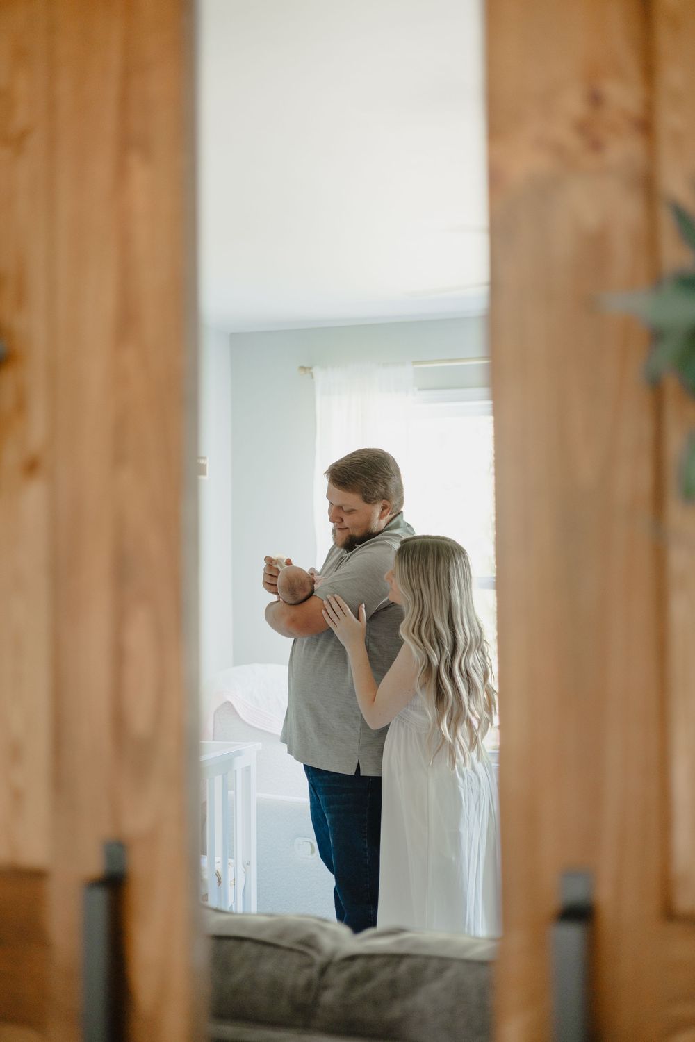 A couple embraces while dancing together in a sunlit room viewed through a wooden doorframe.