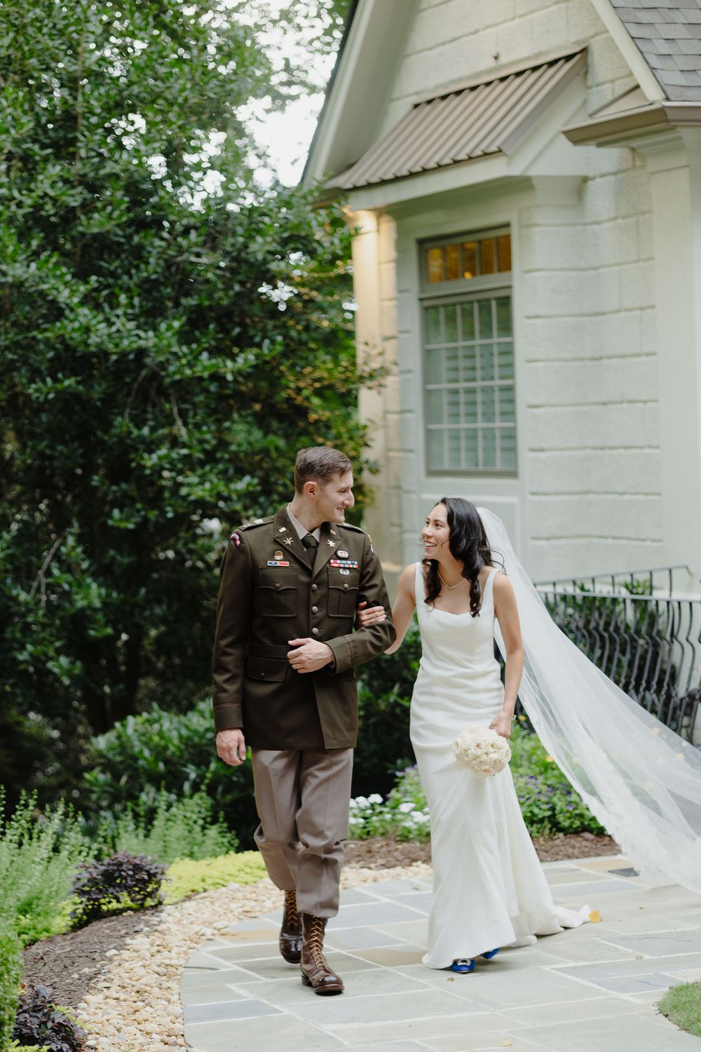 A couple in wedding attire shares a playful moment on stone steps outside a white chapel building.