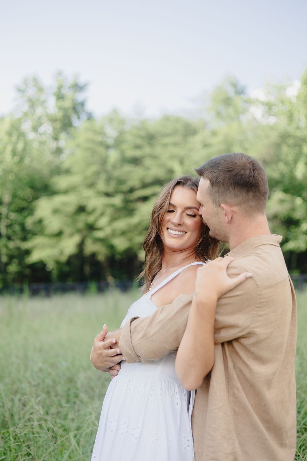 A couple shares joyful moments together in a sunny field wearing neutral colored clothing.