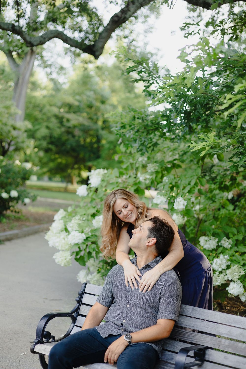 A couple shares an intimate moment while sitting together on a park bench surrounded by green foliage.