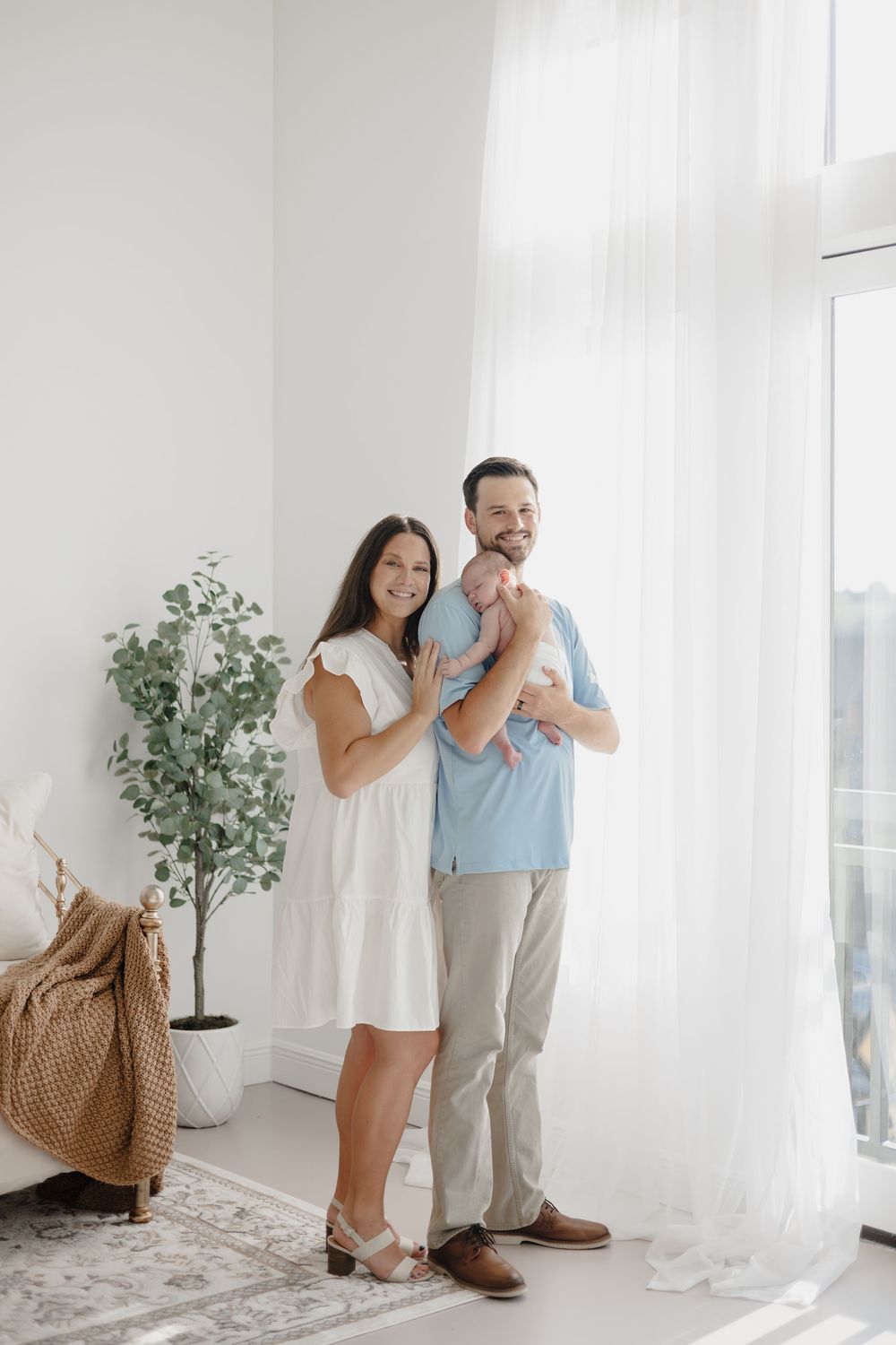 A couple shares tender moments together in a bright white room with potted plants and woven decor.