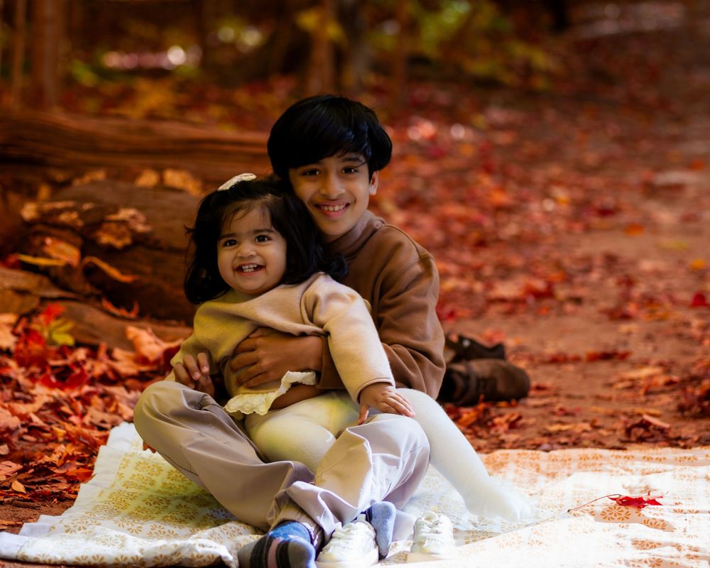Elder brother and little sister enjoying a joyful moment together in an outdoor fall photoshoot, with the vibrant autumn leaves creating