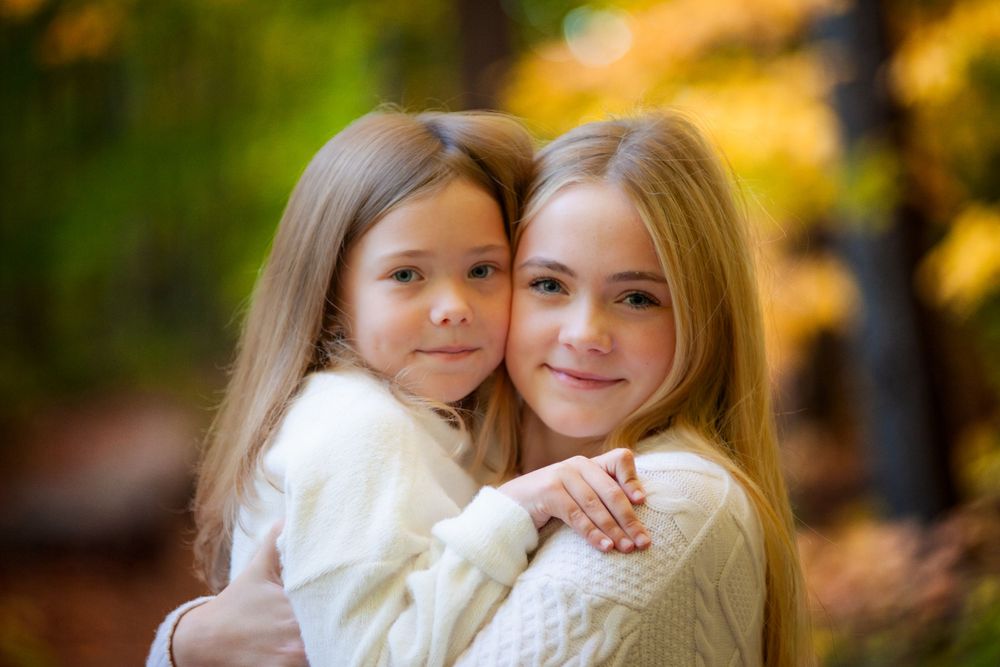 Elder and little sister sharing a special moment together in an outdoor fall photoshoot, surrounded by the vibrant colors of autumn leaves a