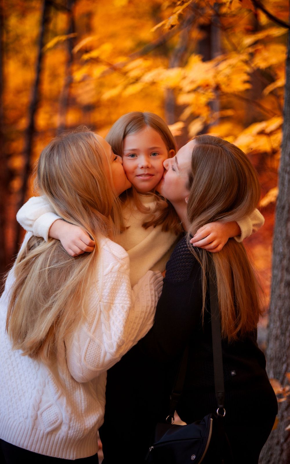 Mother and elder sister sharing a sweet kiss with their little sister, surrounded by a perfect autumn backdrop with colorful fall leaves,
