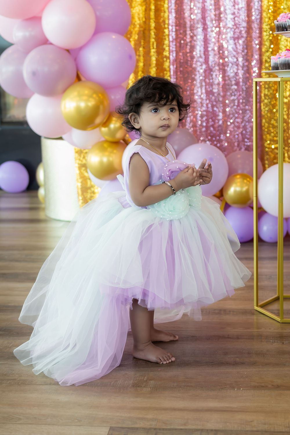 Sweet 1-year-old birthday girl beaming in her party attire surrounded by celebration decor.