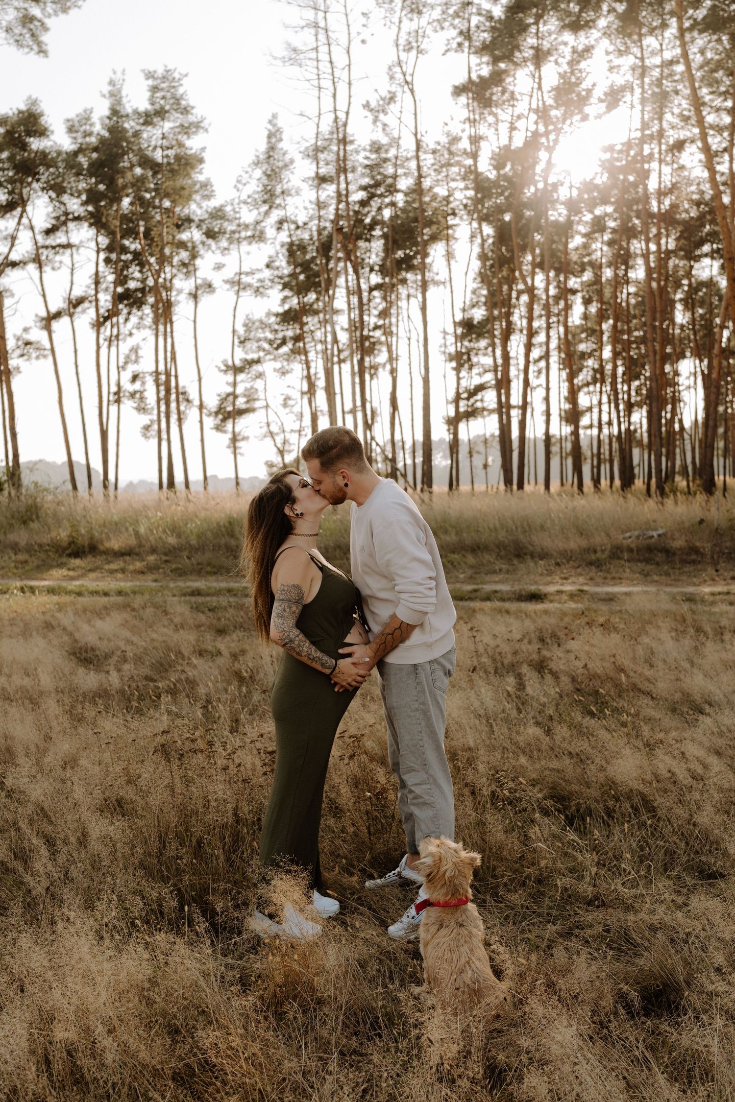 Romantic couple sharing a tender moment in a pine forest at sunset with their dog.