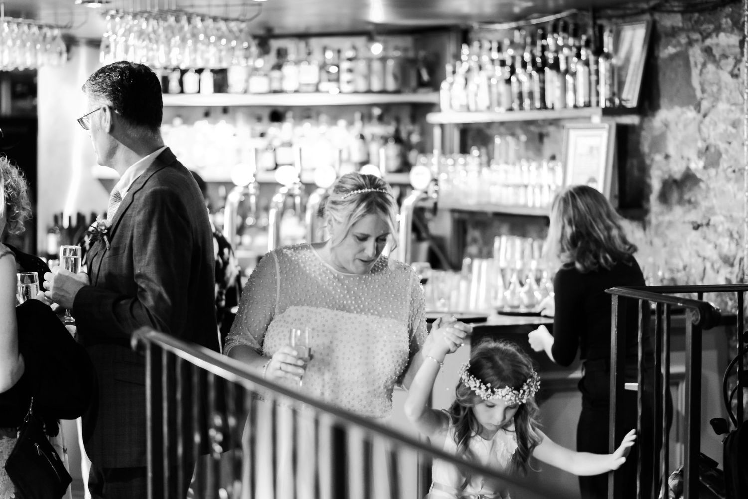Guests enjoying drinks and conversation at a bar with wine glasses hanging overhead.