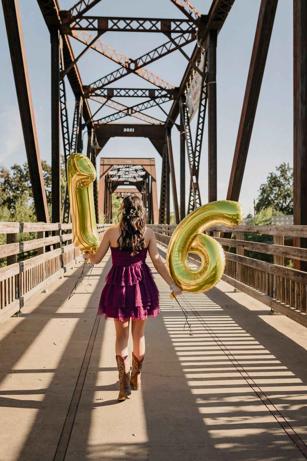 Gold number 16 balloons carried on a rustic bridge in a celebratory pose.