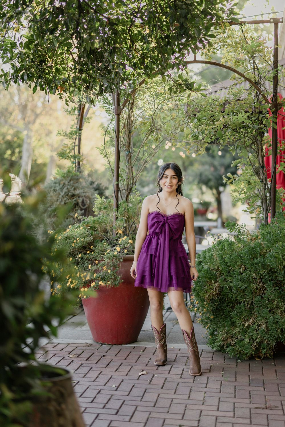 Outdoor fashion photo with purple dress and cowboy boots along garden pathway with red planter.