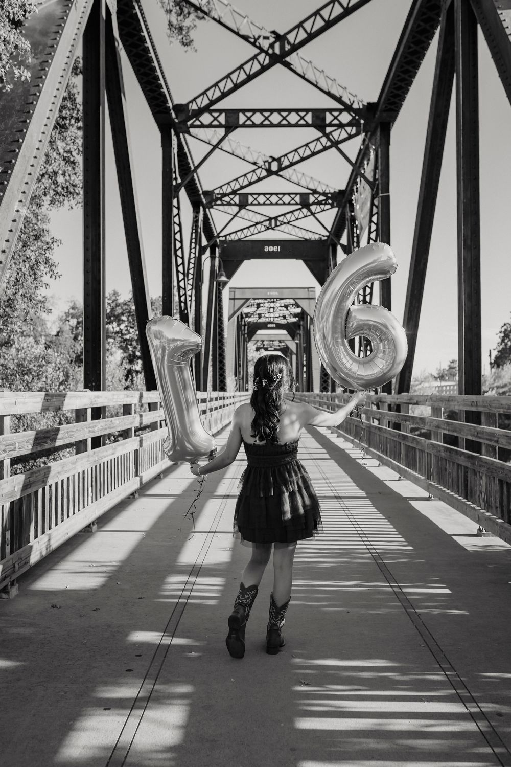Black and white photo of Sweet 16 celebration on historic bridge with metallic number balloons.