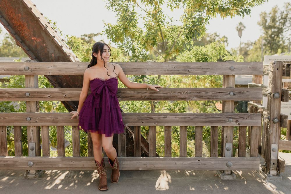 Fashion portrait on wooden bridge featuring purple strapless dress paired with brown western boots.