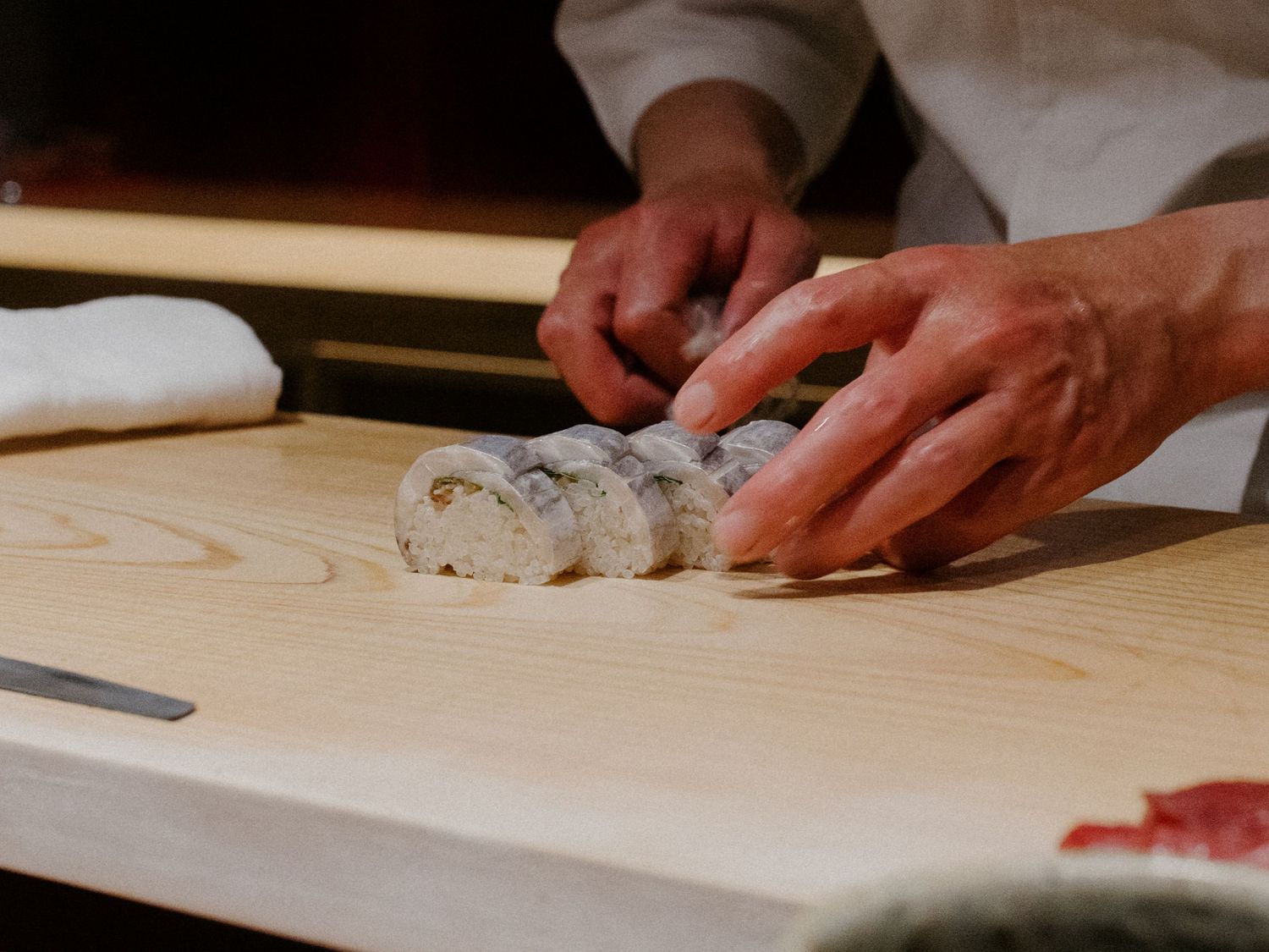 Close-up of hands preparing sushi rolls on a wooden cutting board.