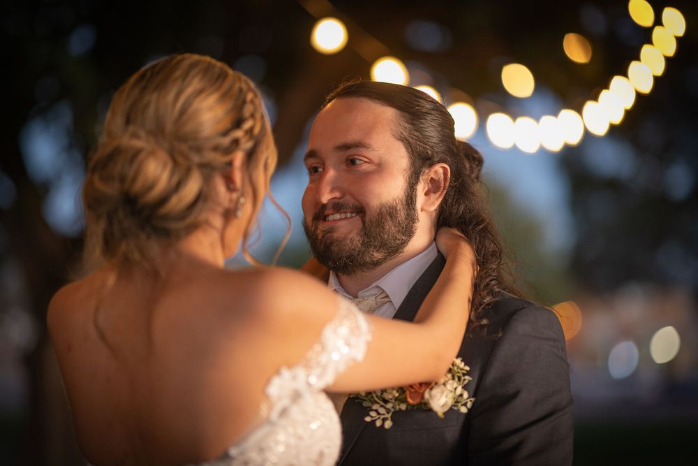 A tender moment between a couple at an outdoor evening wedding with string lights glowing in the background.
