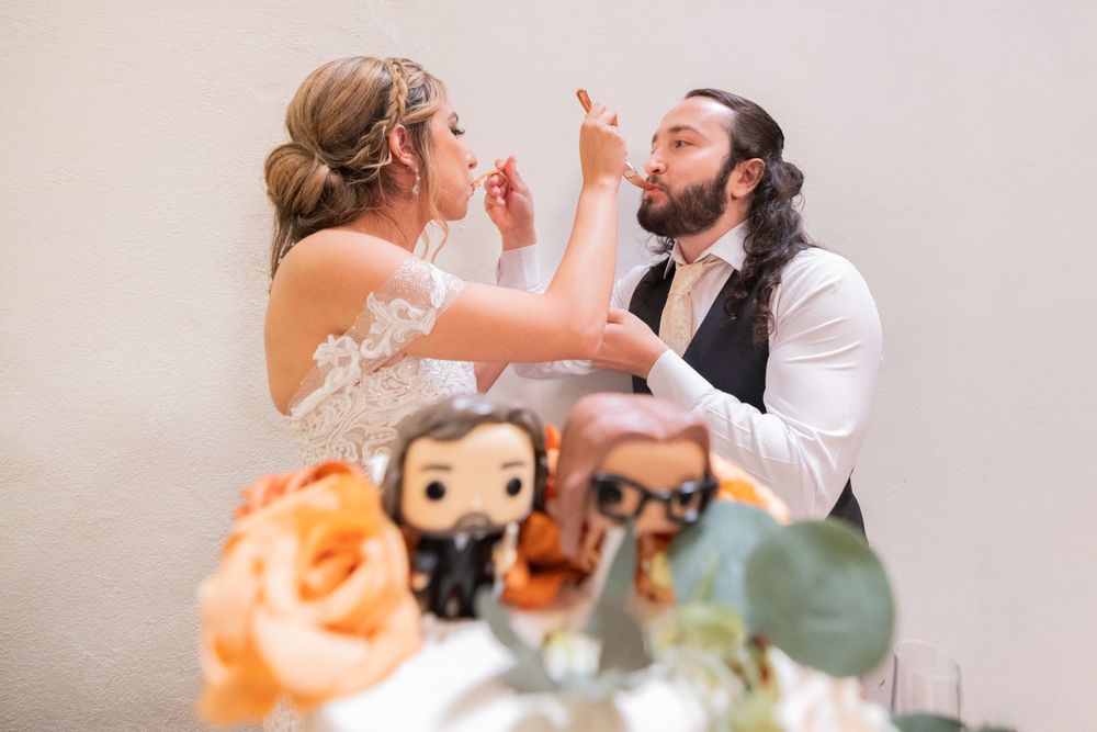Couple shares wedding cake while Funko Pop cake toppers decorate the floral display in foreground.
