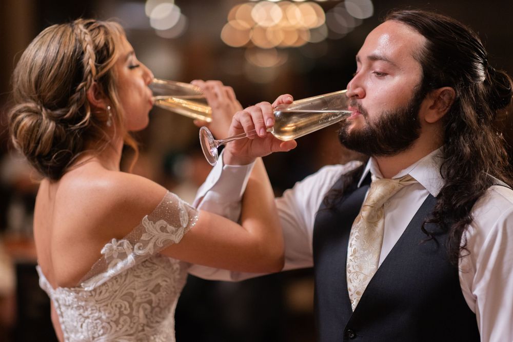 Happy bride and groom drink champagne together with arms linked during their wedding reception celebration.