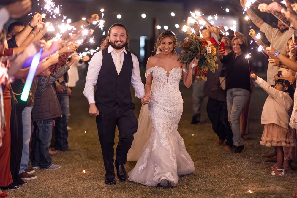 A happy couple walks through a sparkler exit line at their outdoor evening wedding celebration.