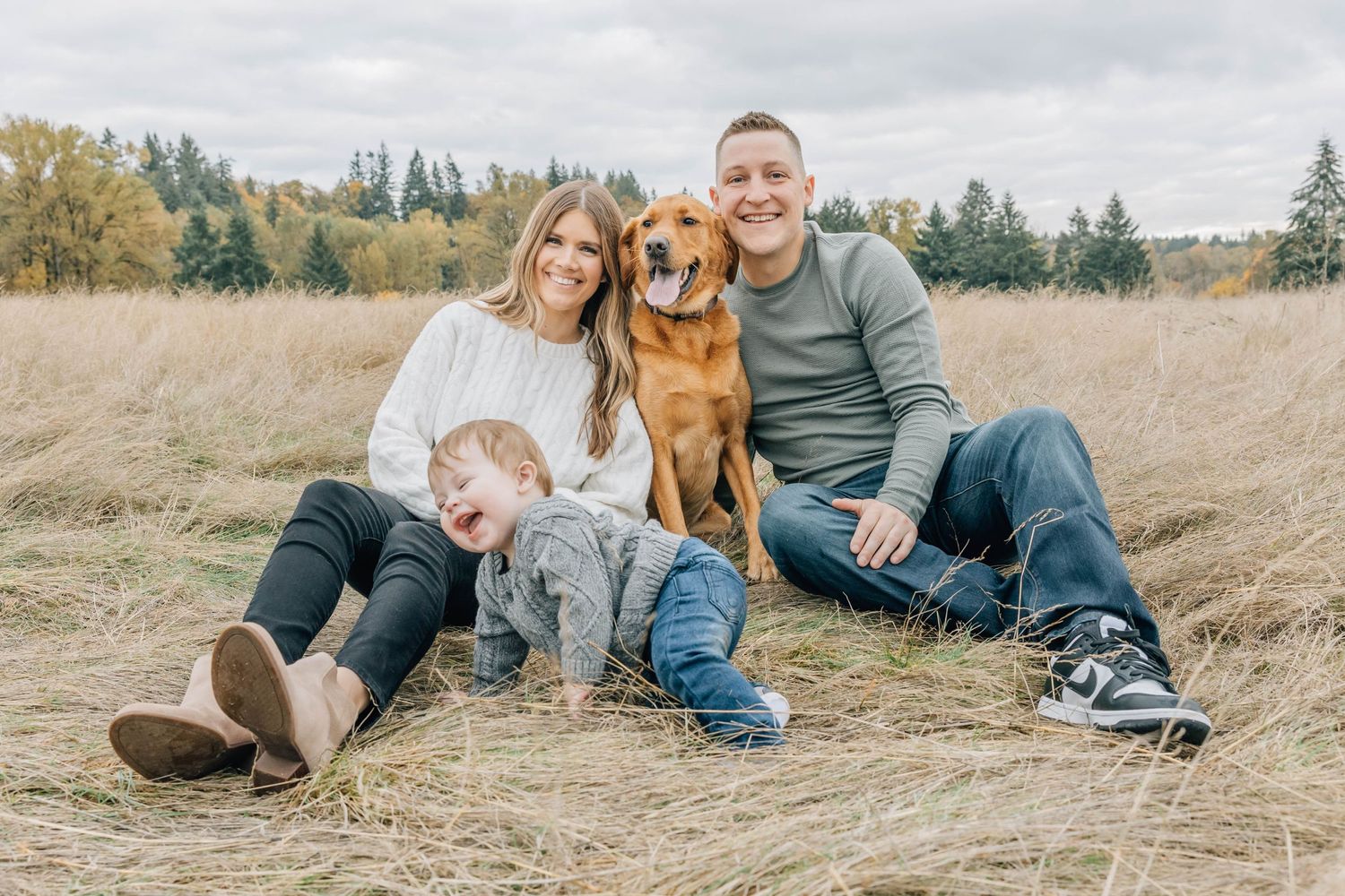 Happy family with golden retriever dog sitting together in golden autumn grass field.