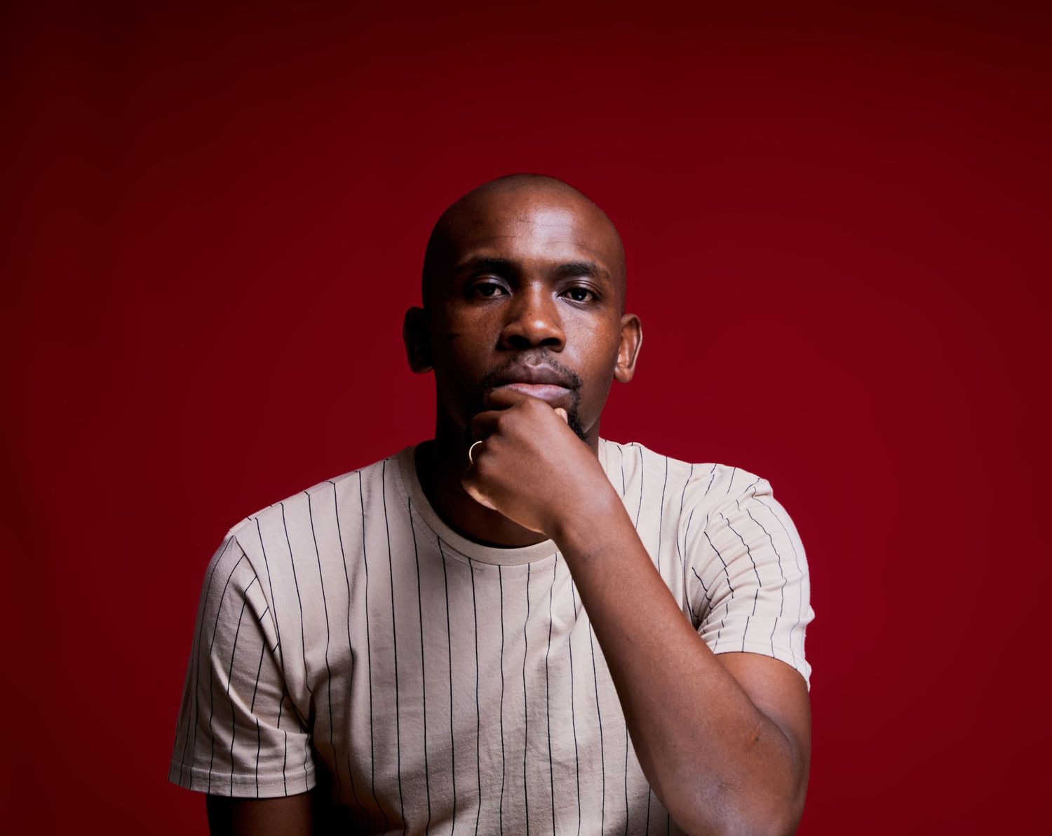 Portrait of person in striped shirt against red background with contemplative expression.