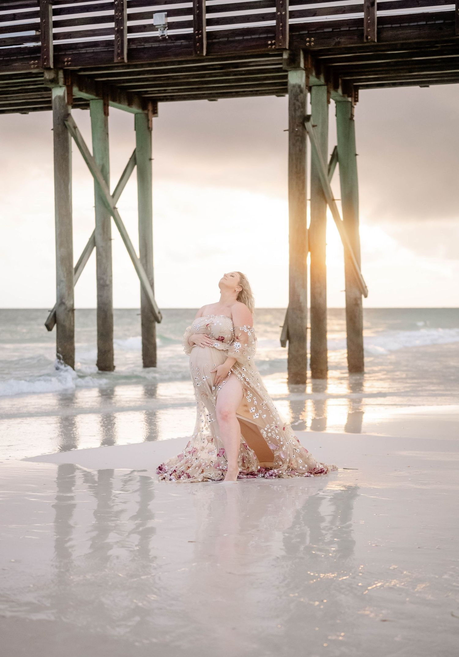 Silhouetted maternity photo under pier with sunlight streaming through.