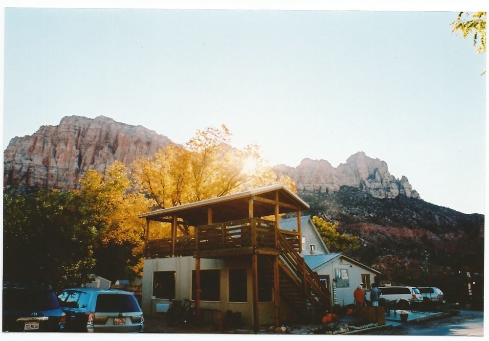 Rustic mountain lodge in Zion National Park with deck against dramatic red rock cliffs at sunset.