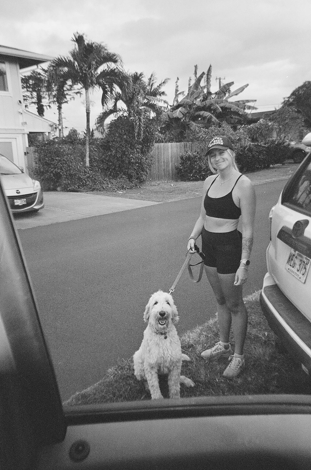 Black and white photo of person walking a fluffy white dog on a residential street.