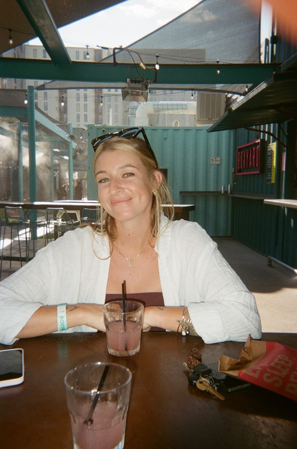 Woman sitting at outdoor restaurant table with drinks enjoying casual dining atmosphere.