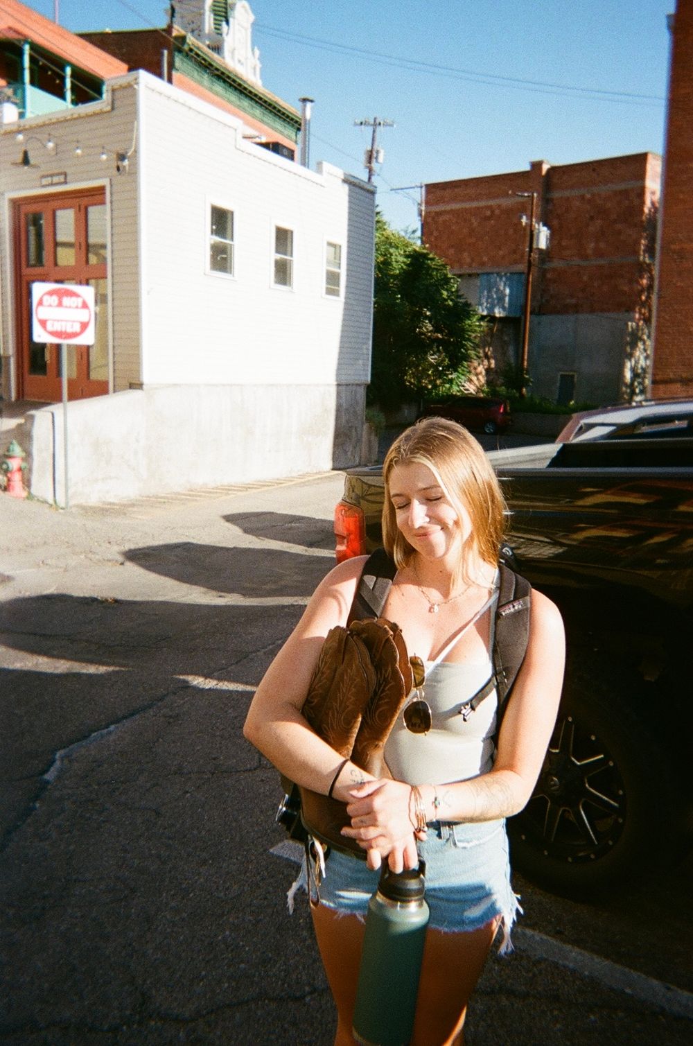 Person in summer outfit standing on urban street corner in bright sunlight.