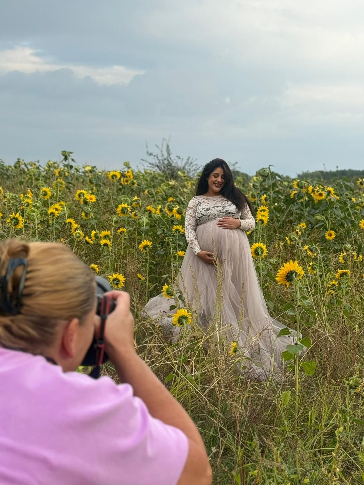 Photographer captures a model in a flowing white dress posing among vibrant yellow sunflowers in a summer field.