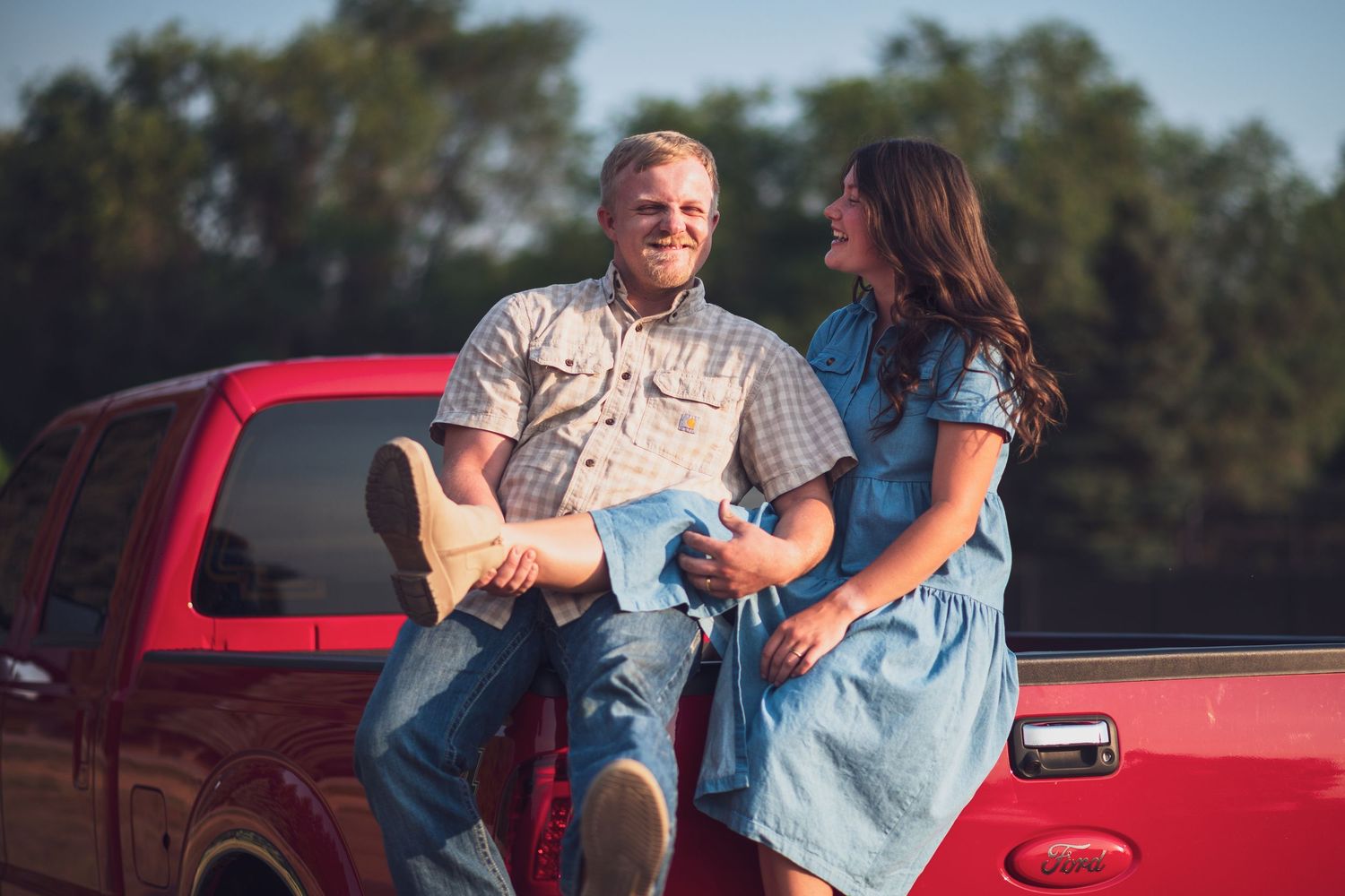 Couple laughing while sitting on the edge of a pickup truck bed.