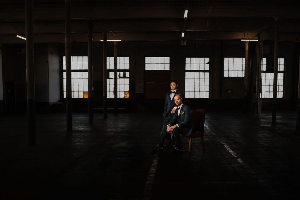 A person sits alone in a dark industrial space with sunlight streaming through large windows.