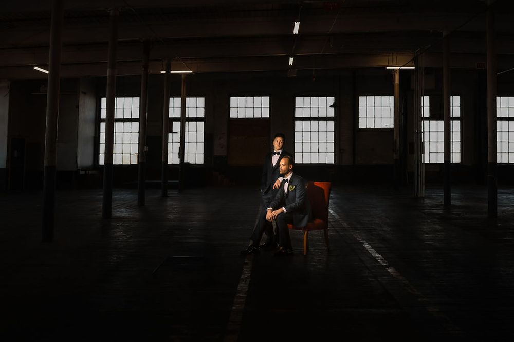 Dark industrial warehouse interior with rows of windows and dramatic lighting creating moody atmosphere.