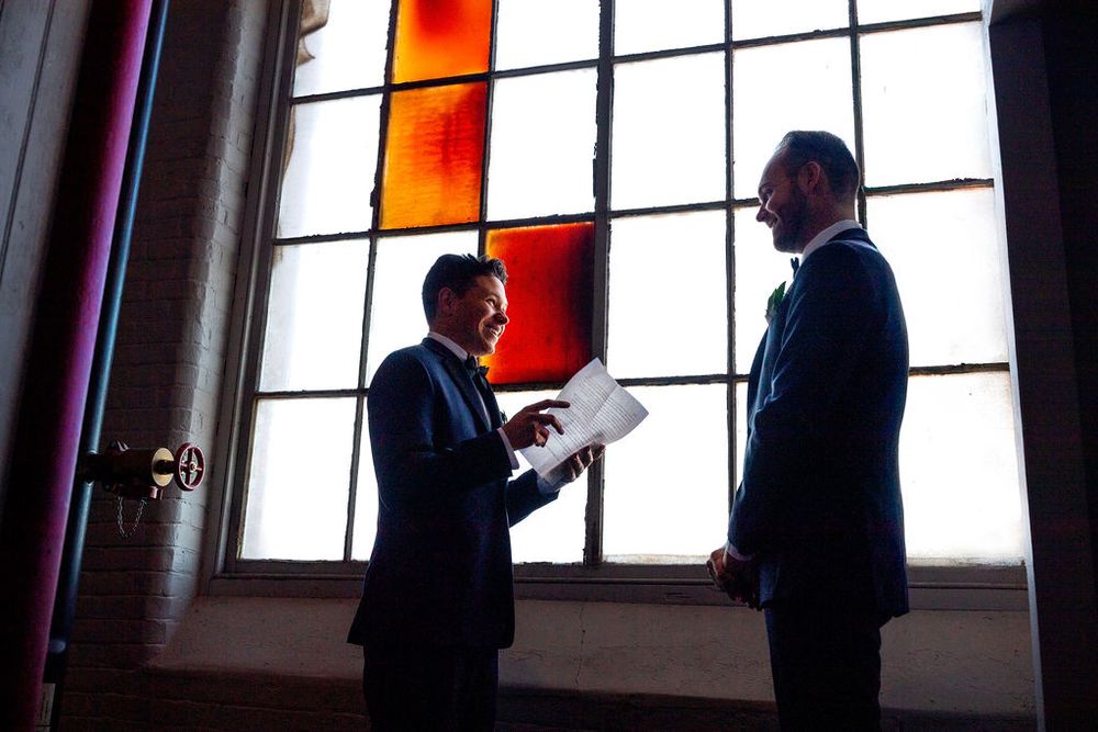 Two people in suits stand in silhouette against a large window with warm colored light.