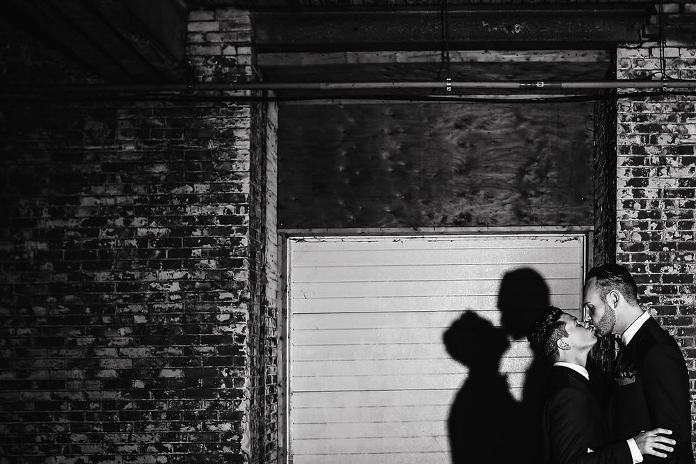 A series of black and white silhouettes against brick walls show intimate moments between couples in an urban setting.