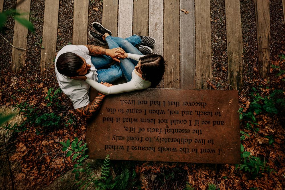 A couple embraces on a rustic wooden deck surrounded by autumn foliage and fallen leaves during a photo session.
