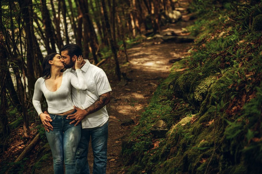 A couple walking together on a sunlit forest path through tall trees and greenery.