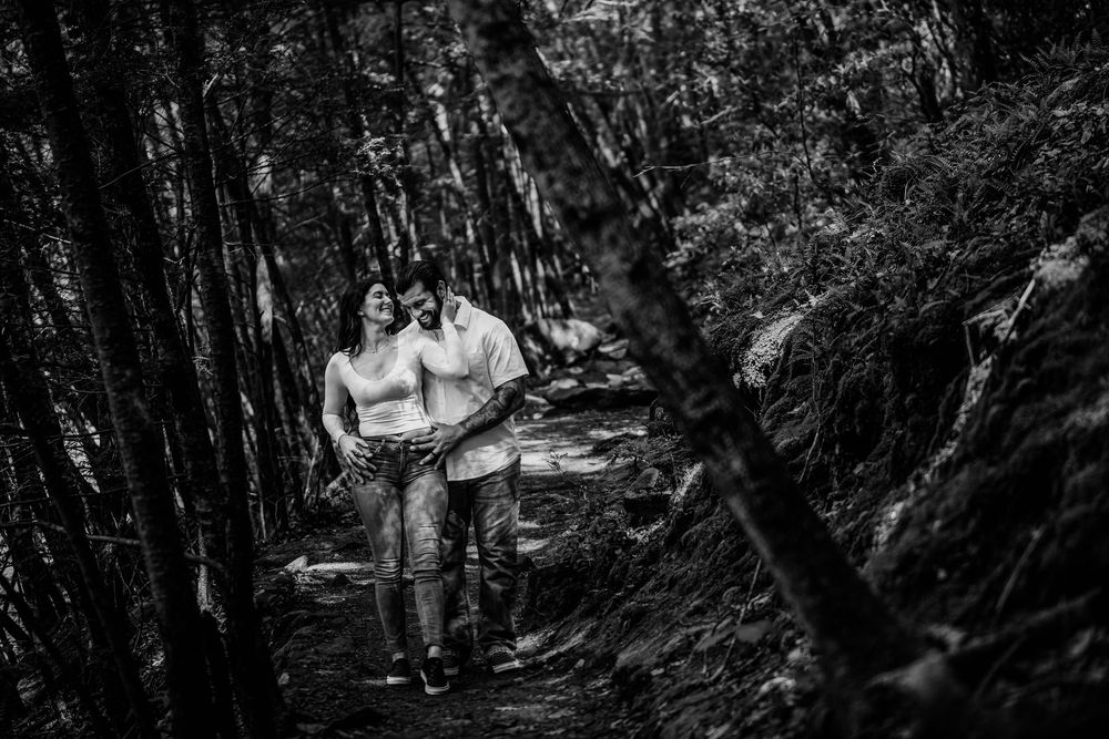 Black and white photograph of people walking through a wooded forest trail with dramatic lighting and shadows.