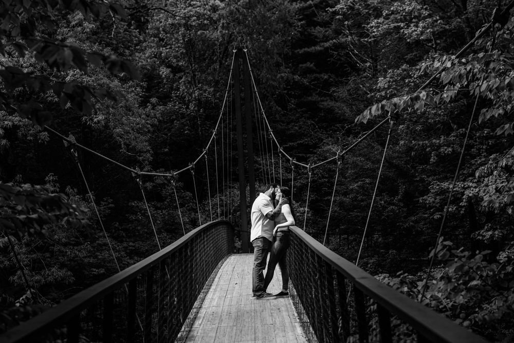 A series of black and white wedding photos showing couples on a rustic suspension bridge in the forest.