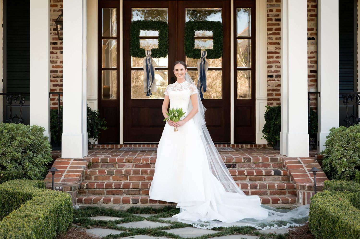 Elegant bridal portrait on brick steps with white columns and glass doors.