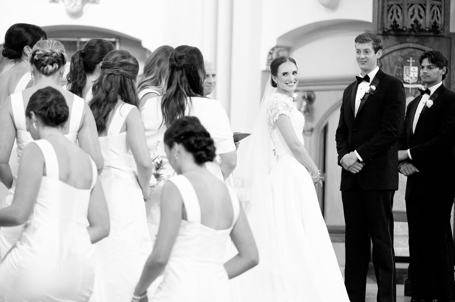 Wedding party in formal black and white attire gathered inside traditional church.