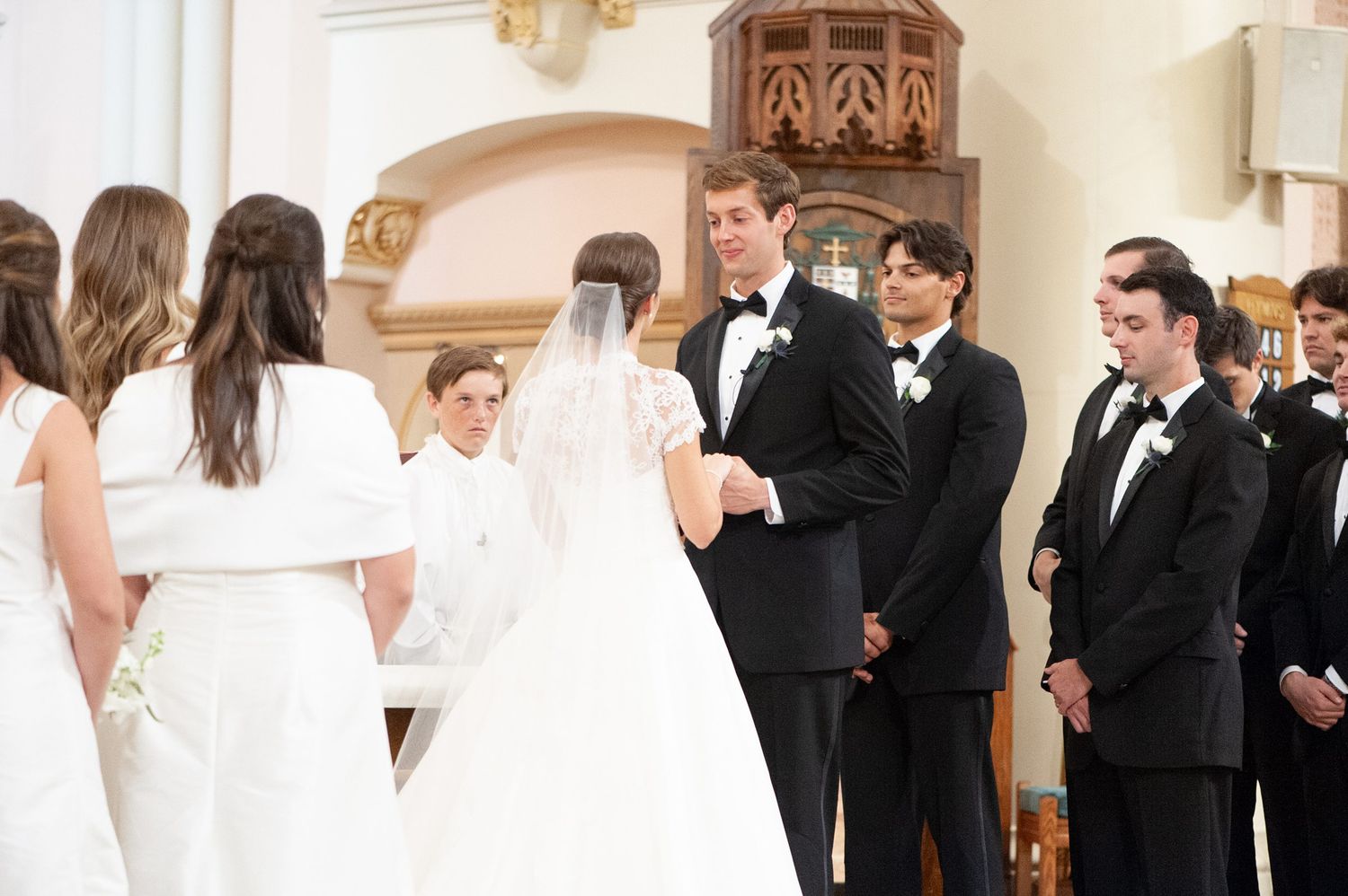 Wedding party members interacting during formal ceremony in traditional church setting.