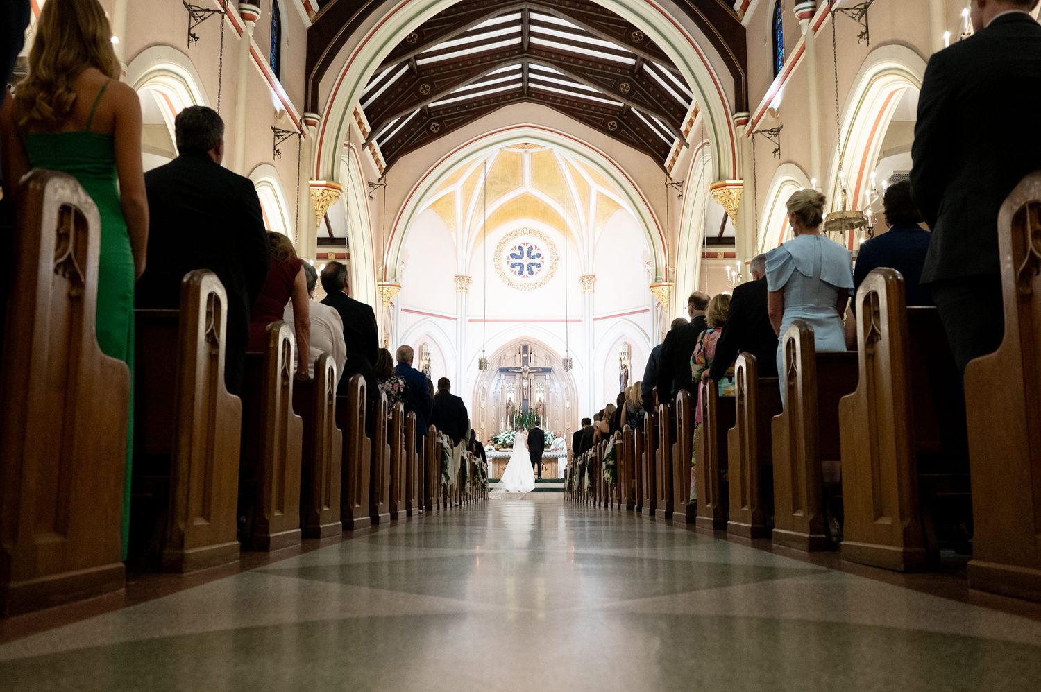 Elegant church interior with vaulted ceilings and wooden pews illuminated by natural light during a wedding ceremony.