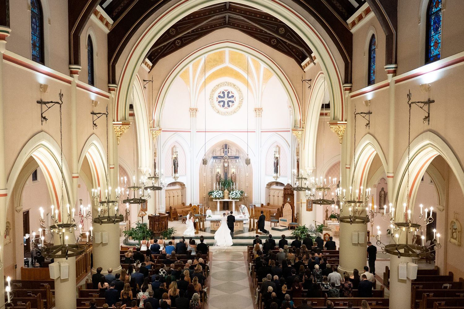 Panoramic view of a grand church interior with gothic arches and ornate altar during a wedding celebration.