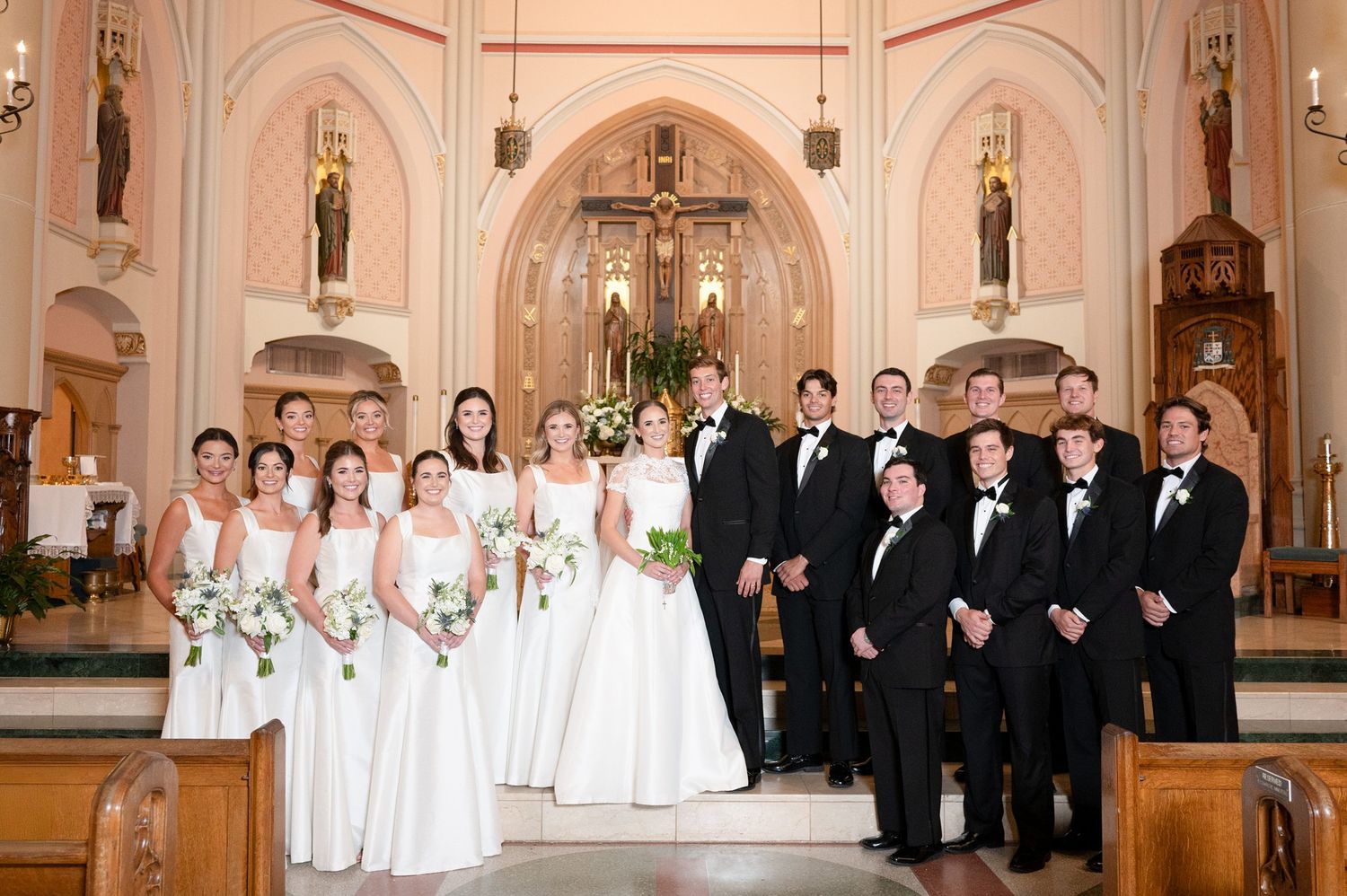 Wedding party lined up in formal attire inside an ornate church with classical architecture.