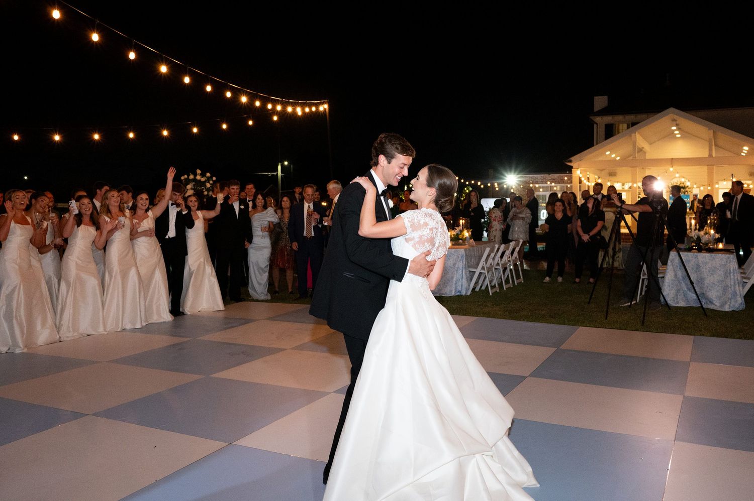 Wedding reception dance floor under string lights with guests celebrating.